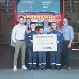 Vier Männer in schicker Kleidung stehen neben drei Kindern der freiwilligen Feuerwehr, die Kinder halten einen mycity & froneri Spenden Check über 1000 Euro in der Hand.