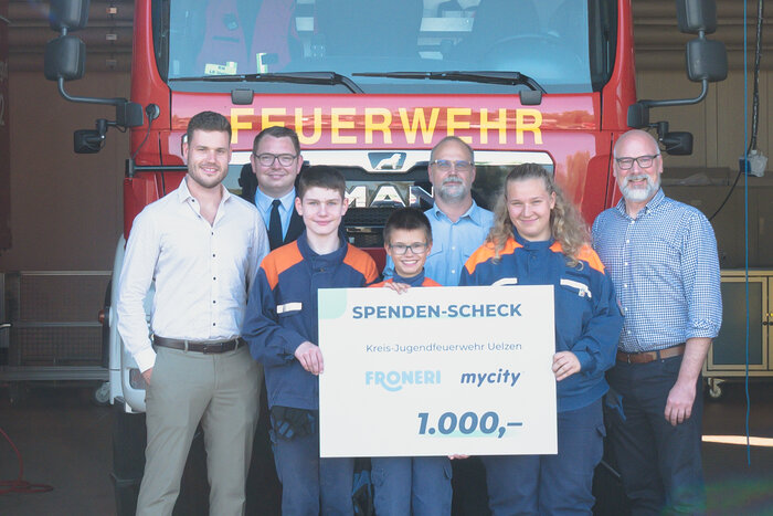 Vier Männer in schicker Kleidung stehen neben drei Kindern der freiwilligen Feuerwehr, die Kinder halten einen mycity & froneri Spenden Check über 1000 Euro in der Hand.