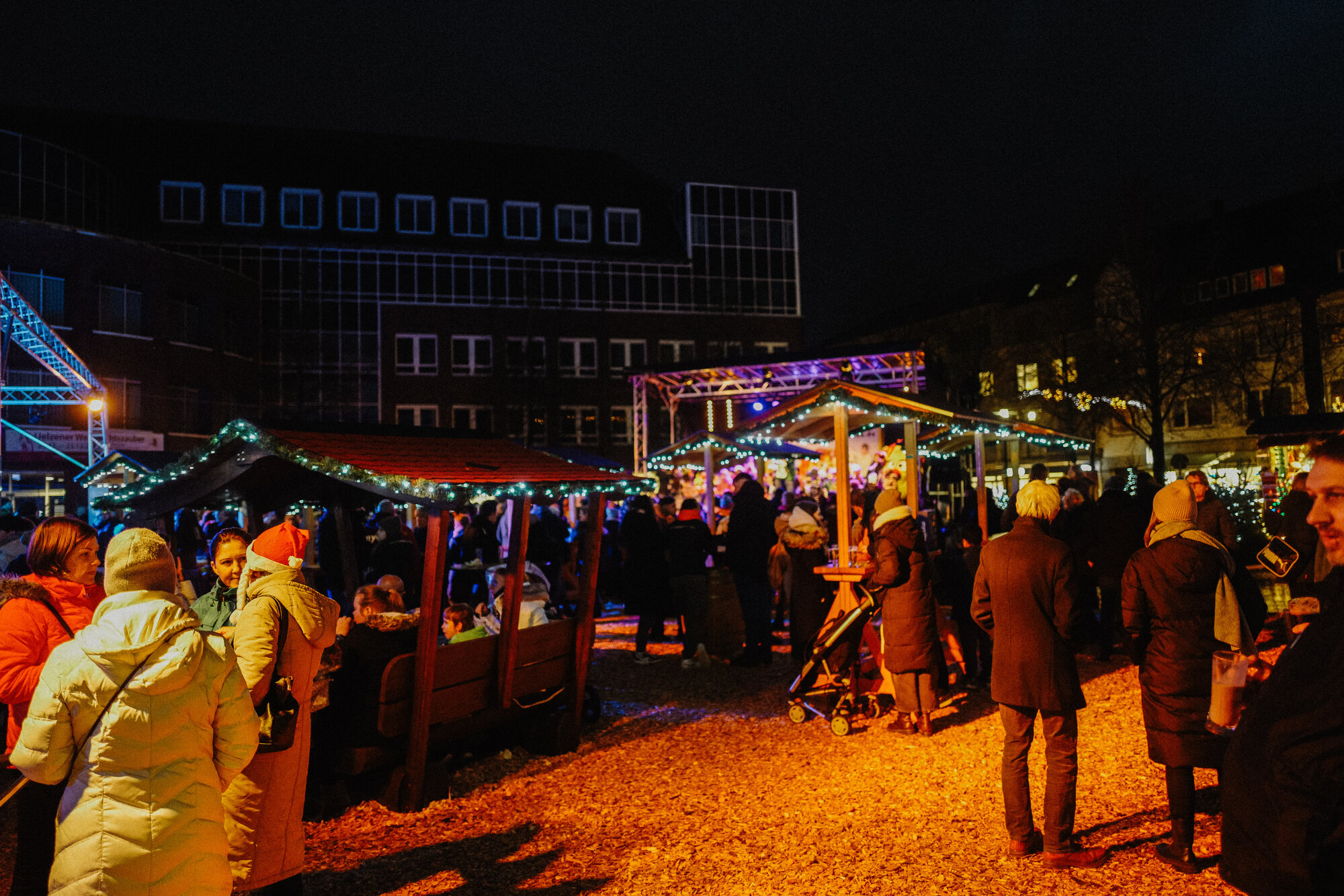 Aufnahme des Geschehens bei einem Weihnachtsmarkt, es stehen viele Menschen um Stände versammelt.