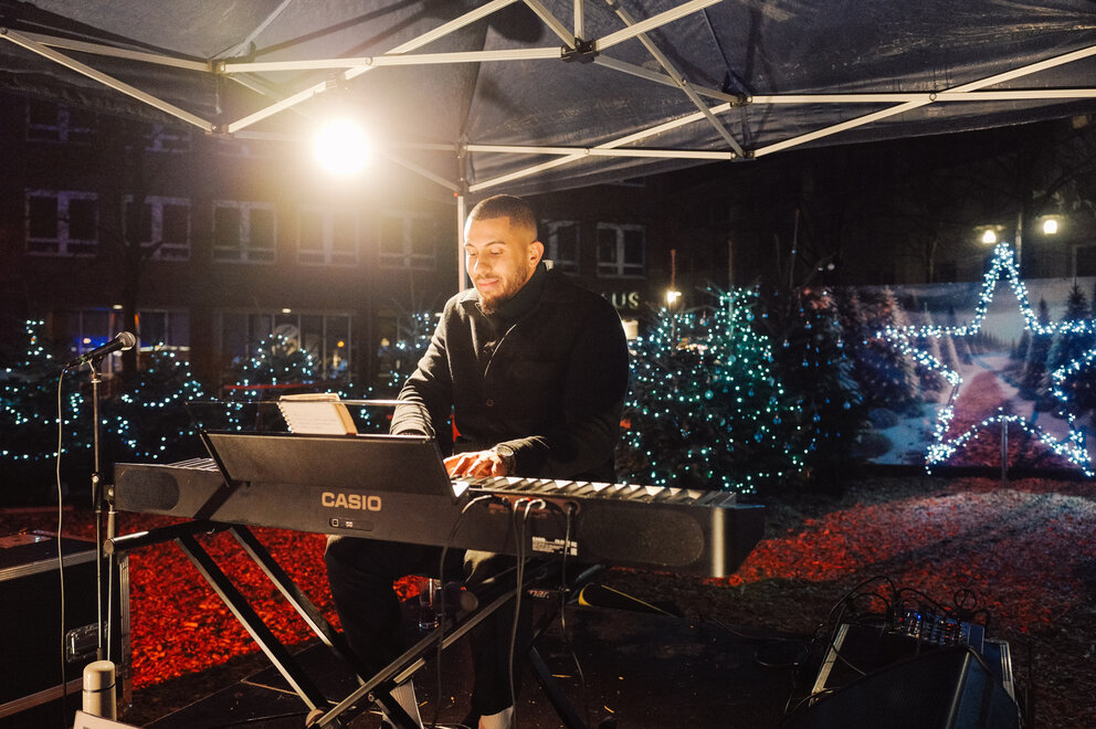 Ein Mann steht an einem Casio Keyboard, im Hintergrund weihnachtliche Lichter.