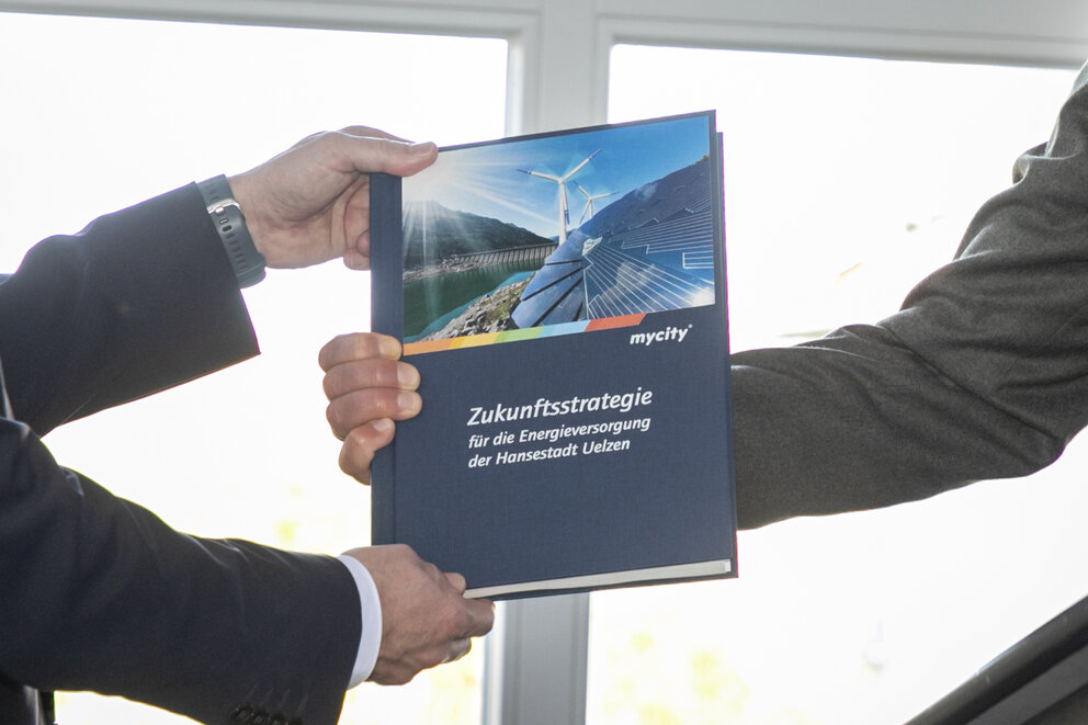 Zwei Menschen halten ein Buch in die Kamera mit der Aufschrift "Zukunftsstrategie für die Energieversorgung der Hansestadt Uelzen