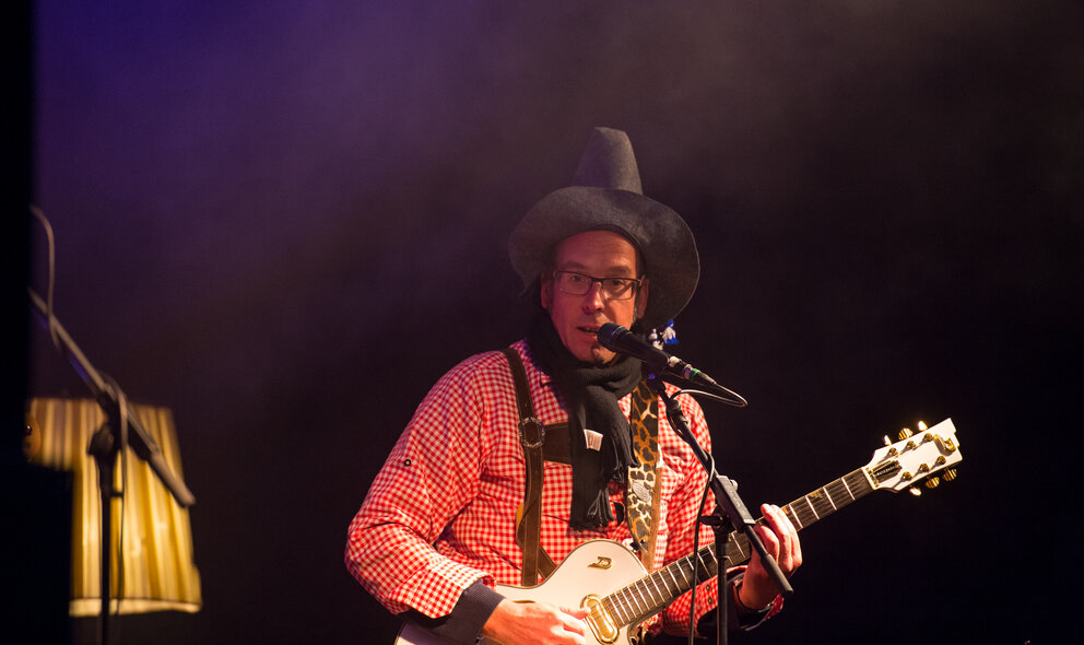 Ein Mann spielt Gitarre und singt dabei ins Mikrofon, er hat eine Zipfelmütze auf.