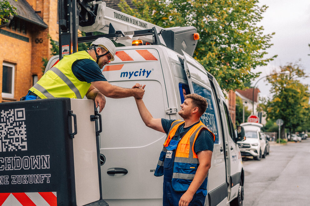 Zwei mycity Techniker geben sich einen Handschlag vor einem mycity Baustellenfahrzeug