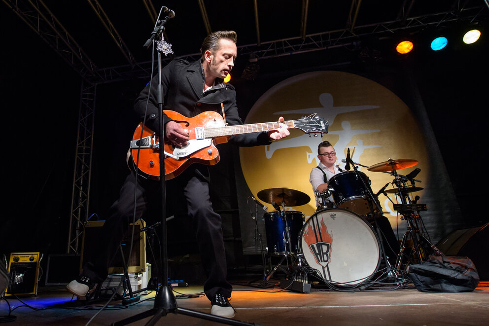 Aus der ersten Reihe Nahaufnahme einer Band mit Fokus auf den Frontmann mit E-Gitarre und den Drummer.