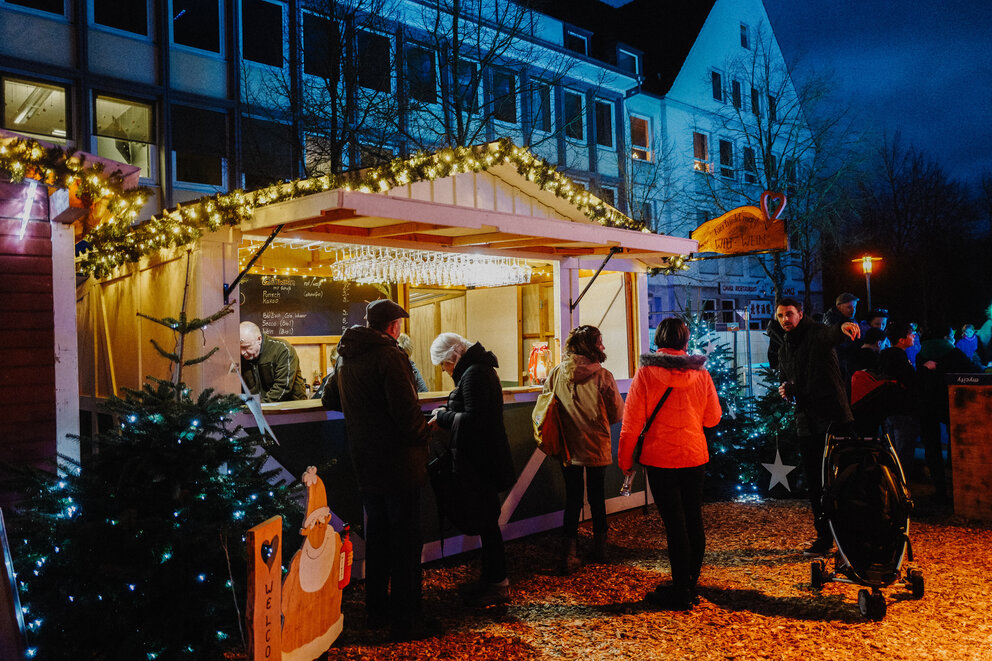 Einige Leute stehen an einem beleuchteten Weihnachtsmarkt Stand 