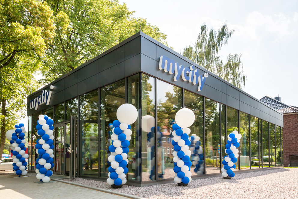 Ein komplett verglastes Gebäude, das mycity Service Center, mit vielen weißen und blauen Luftballons an den Fenstern.