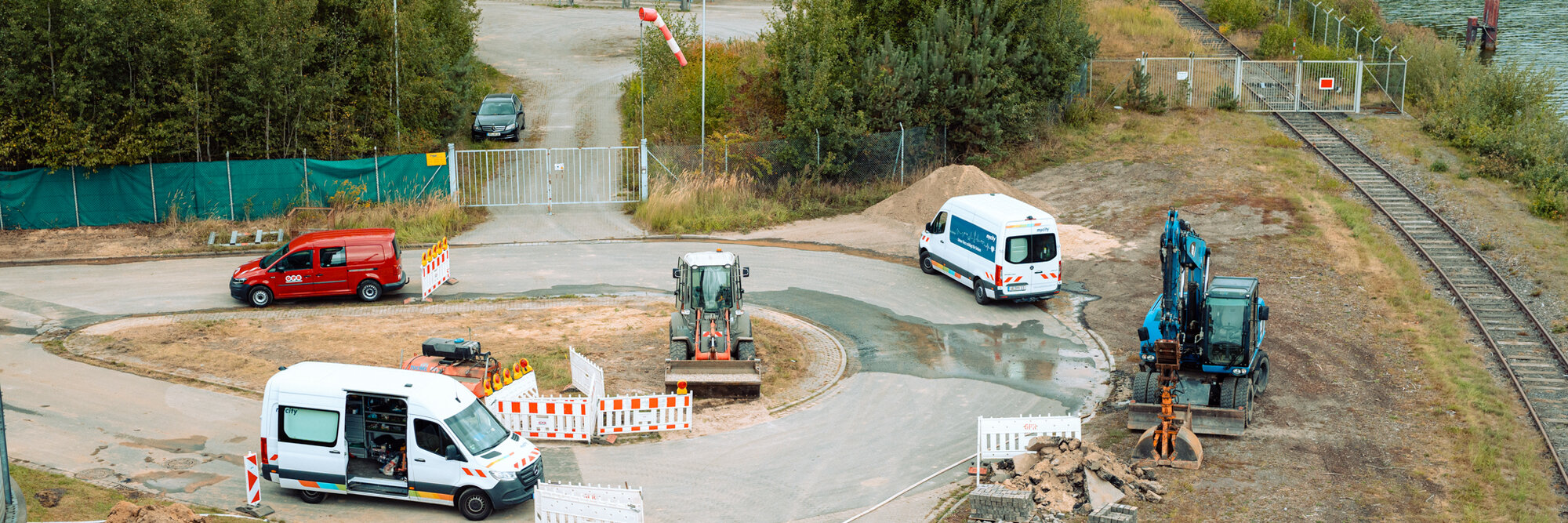 Mehrere mycity Baustellenfahrzeuge stehen an einer Baustelle an einem Kreisverkehr. Einige Baustellenschilder stehen nebendran.