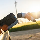 Nahaufnahme eines aufgeklappten Tankdeckels in den ein Ladekabel eingesteckt wird. Im Hintergrund steht ein Winterrad