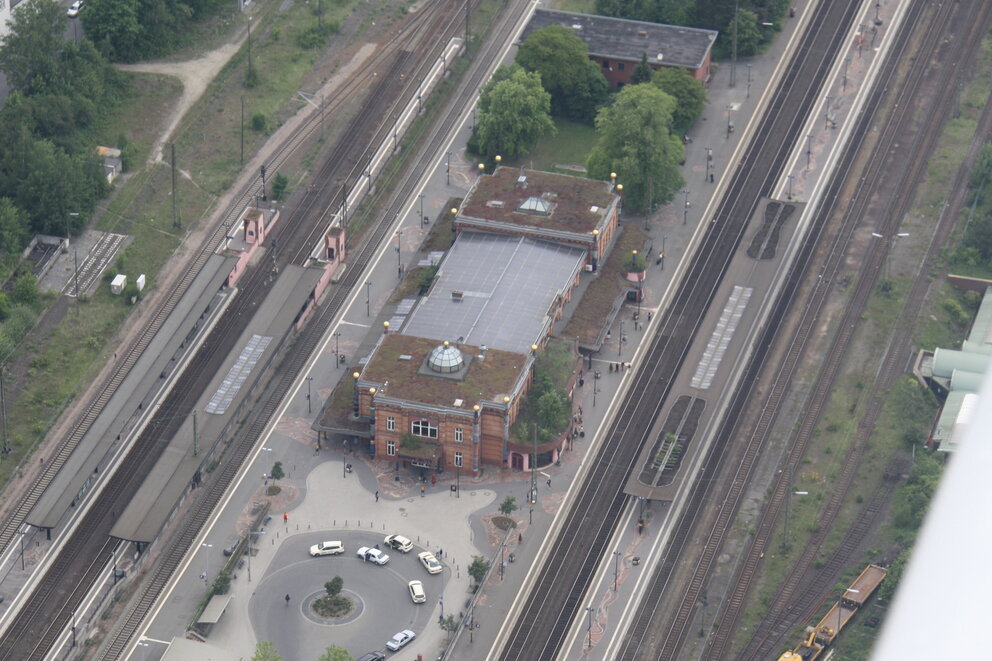Aus der Vogelperspektive Bahnschienen und daneben ein Gebäude und ein Kreisverkehr.