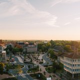 Luftaufnahme der Uelzener Skyline mit Häusern, Marktplatz & Kirche zwischen vielen Bäumen, im Hintergrund ein hellblauer Horizont mit hellem Sonnenschein.
