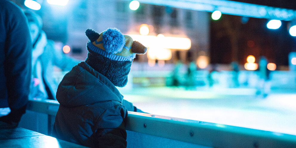 Ein Junge steht am Rand einer Eisbahn und schaut darauf.