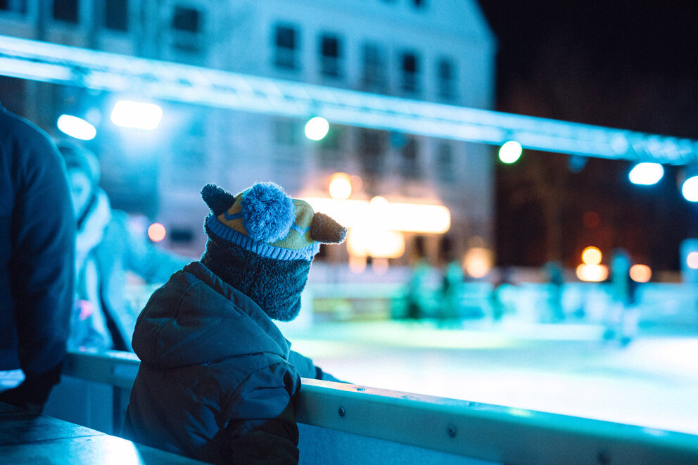 Ein Junge steht am Rand einer Eisbahn und schaut darauf.