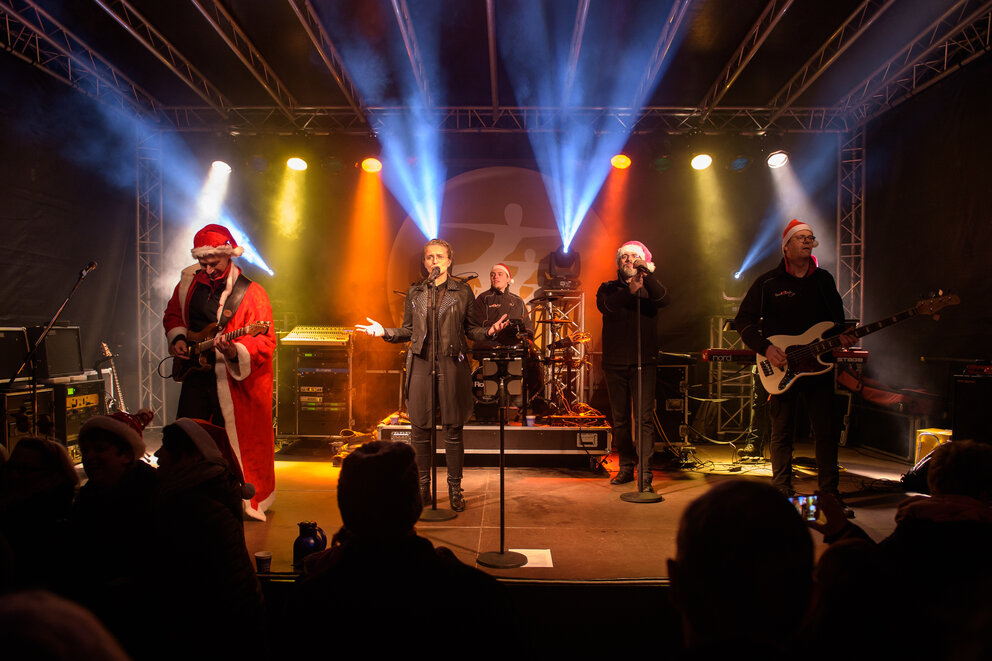 Einer Band mit mit Weihnachtsmützen auf. Sie singen etwas ins Mikro.