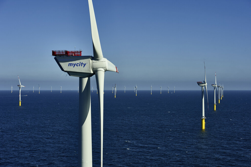 Nahaufnahme eines Wasser Windkraftwerks, im Hintergrund sind einige weitere Windkraftwerke im Wasser zu sehen.