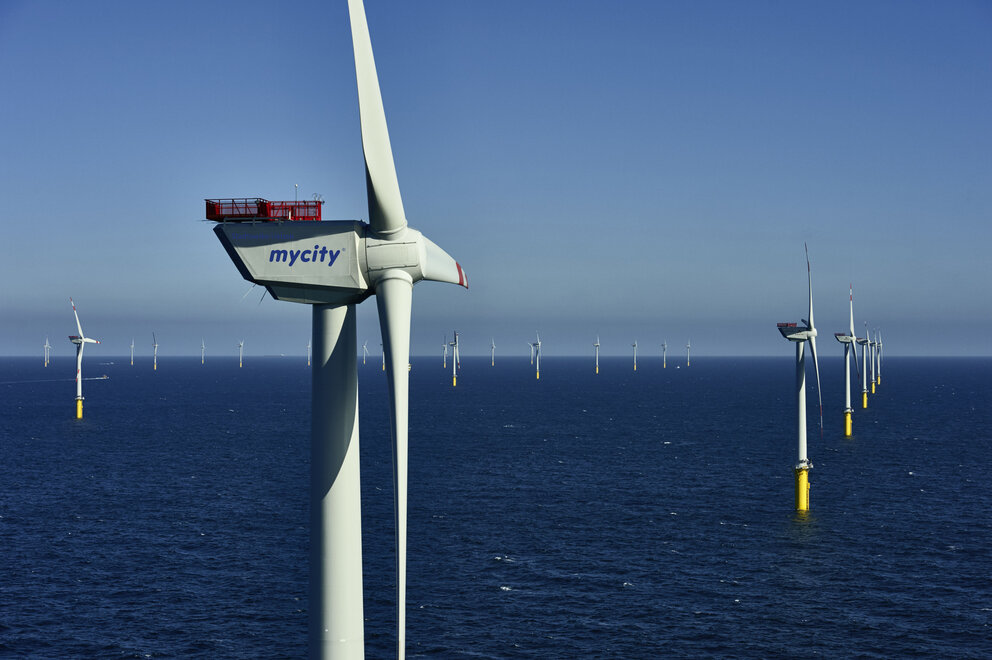 Nahaufnahme eines Wasser Windkraftwerks, im Hintergrund sind einige weitere Windkraftwerke im Wasser zu sehen.