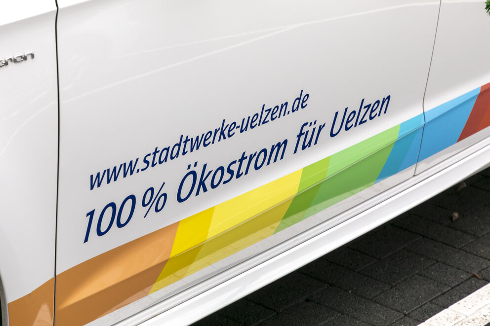 Eine Nahaufnahme einer Einstiegleiste eines weißen Bullis mit Schriftzug 100% Ökostrom für Uelzen und bunten Farben darunter.