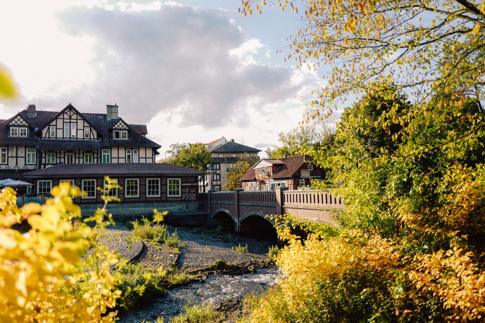 Eine Aufnahme eines Bachs mit einer großen Steinbrücke darüber und einigen Häusern im Fachwerk Stil daneben.