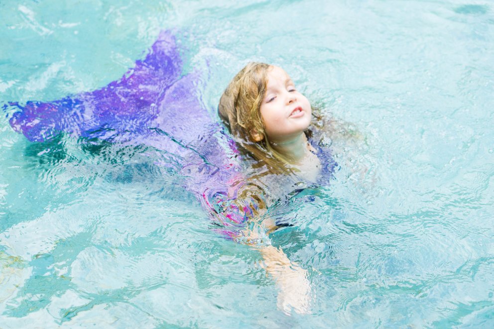 Ein Mädchen ist im Wasser mit einem Meerjungfrauen Kostüm.